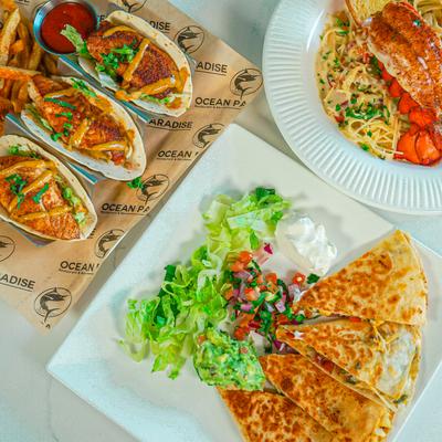Fish tacos, quesadillas, and pasta seafood dish on a table.