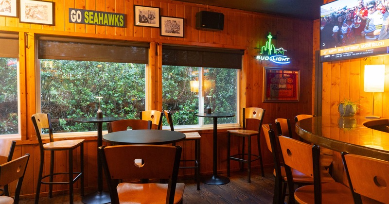 Seating area with tables and bar stools, a large TV screen, and a bar