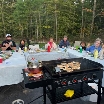 People at an outdoor birthday gathering with a grill and trees in the background.
