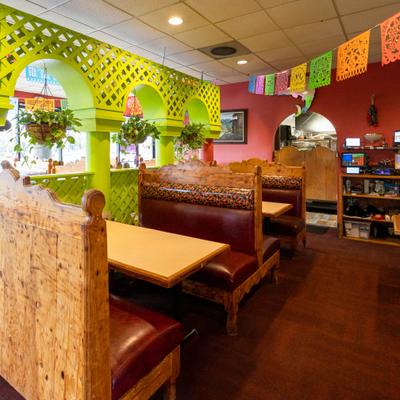 Restaurant interior with booth seating, vibrant green arched wall, and papel picado banners.