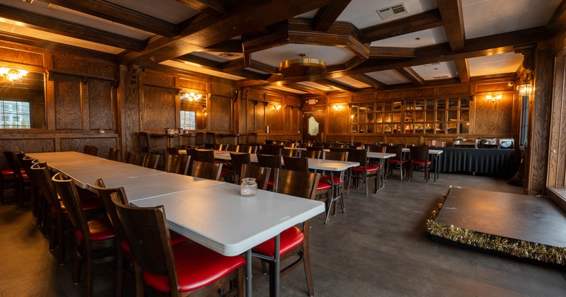 A warm, wood-paneled dining room with long tables, wooden chairs with red cushions