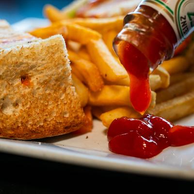 Close-up of a plate featuring fries, sandwich, and ketchup being poured.