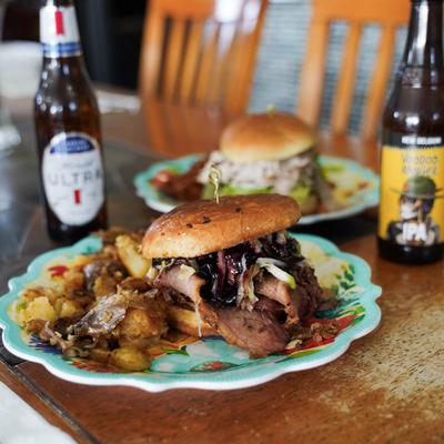 Smoked brisket sandwich with crispy smashed potatoes, accompanied by two beers.