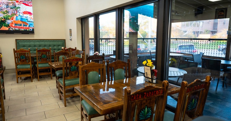 Interior of a restaurant with wooden chairs and tables, large windows, and patio view.