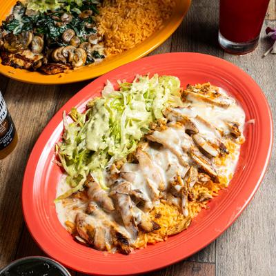 Grilled chicken with creamy sauce, rice, and lettuce with a dressing, served on a red plate.