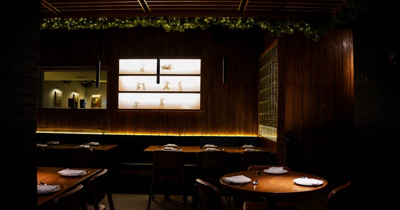 Dimly lit interior with wooden tables, soft lighting and decorative shelves.