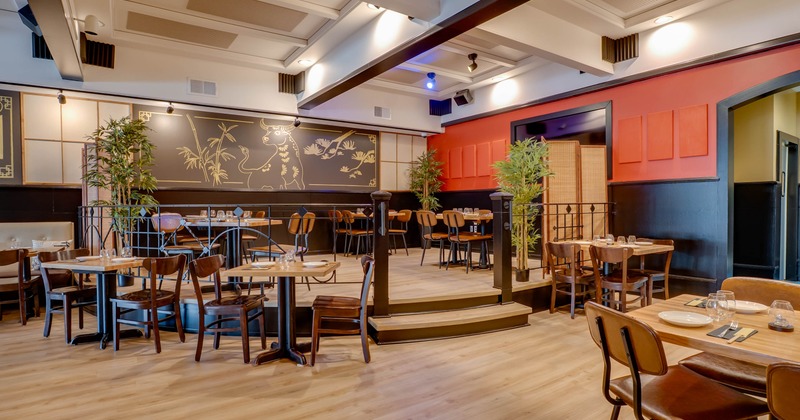 A stylish interior - wooden tables, brown chairs, a decorative black-gold panel wall; bamboo plants