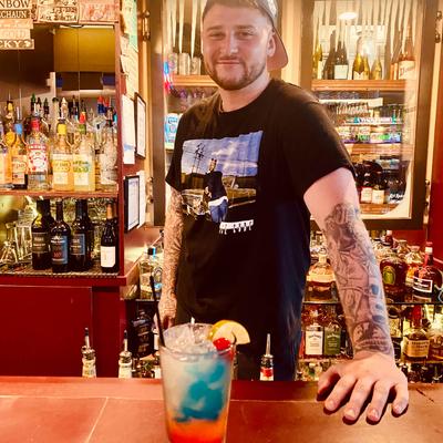 A person standing behind a bar counter with liquor bottles in the background.