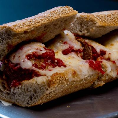 Halved meatball sandwich topped with melted cheese and tomato sauce on homemade seeded bread.