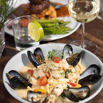 Seafood linguine accompanied with a glass of white wine, a cocktail and, a filet plate.