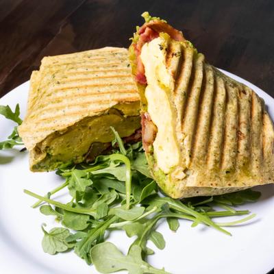 Breakfast panini wrap sliced in half and served on a bed of arugula.