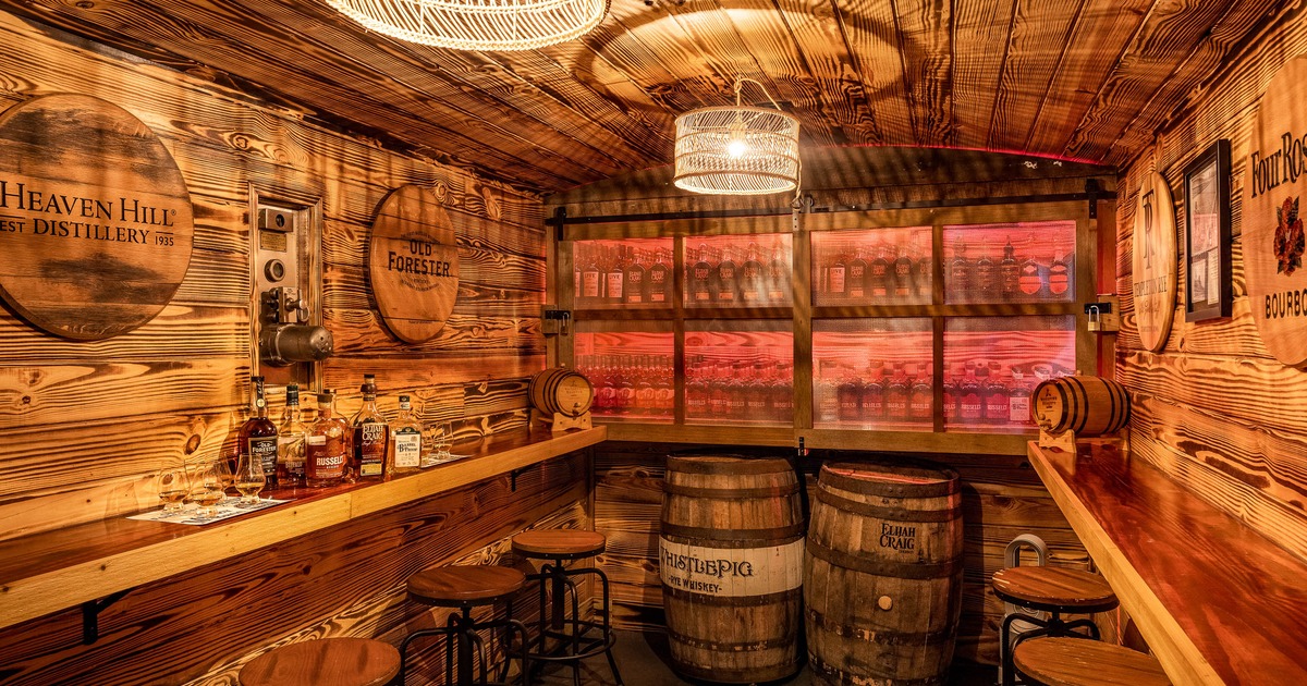 Rustic whiskey bar with wooden walls, barrels, and bar stools