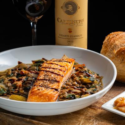 Salmon Con Lenticchie served alongside bread, bottle and glass of red wine.