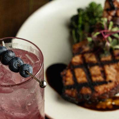 Blueberry cocktail with a grilled pork chop in the background.
