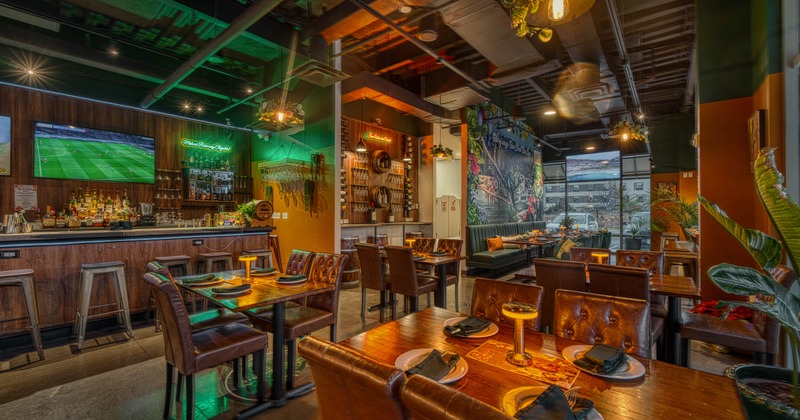 Modern restaurant interior with wooden tables, leather chairs, a bar, a mural, and large windows