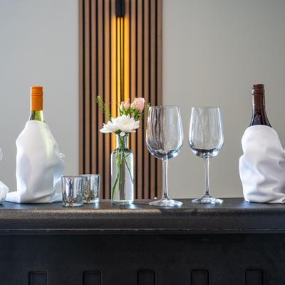 Wine bottles wrapped in white cloth beside empty wine glasses.