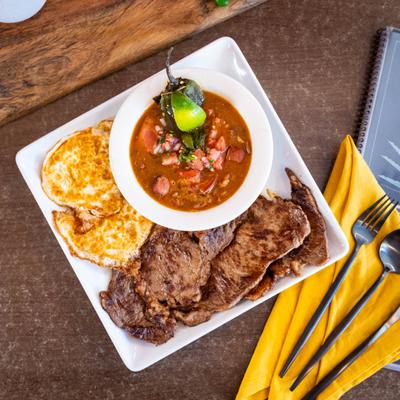 Grilled steak with fried eggs and a bowl of bean soup.