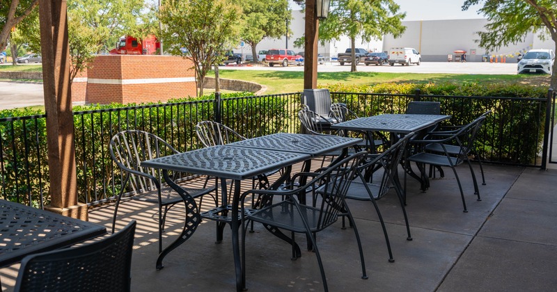 Outdoor patio with black metal tables and chairs, surrounded by a green hedge