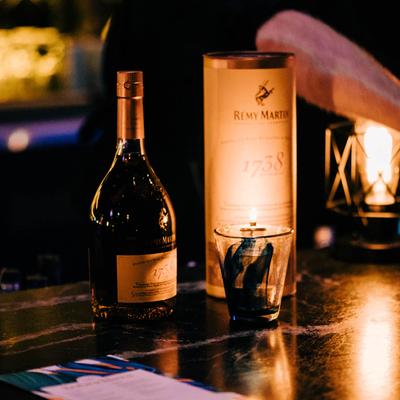 A bottle of cognac and its box on a counter next to a lit candle.