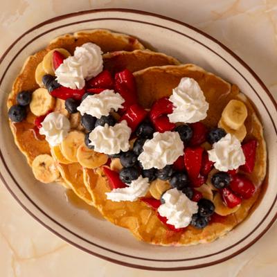 Pancakes topped with strawberries, bananas, blueberries, whipped cream.