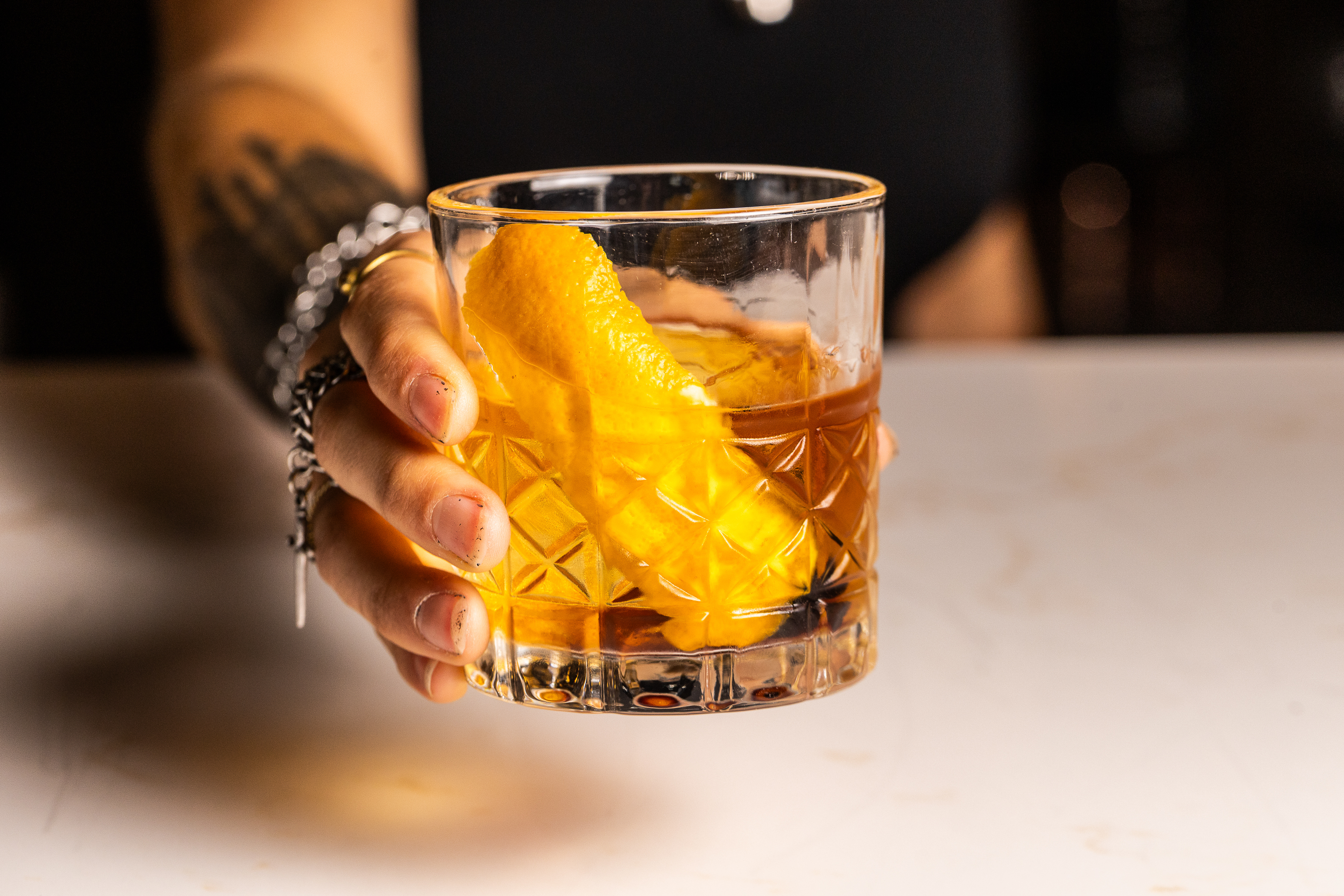 Person holds an old fashioned cocktail with orange peel