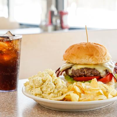Cheeseburger served with potato salad and chips, alongside iced drink.