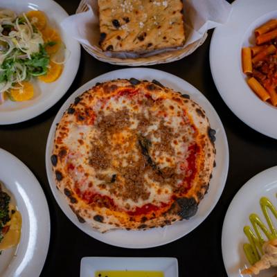Table spread featuring a whole pizza served alongside pasta, focaccia and a salad.