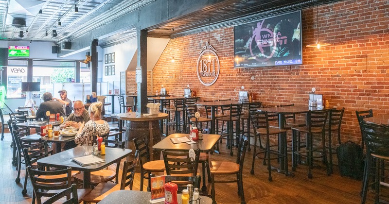 Interior view of dining area with exposed brick walls, tables, chairs, and a large screen TV