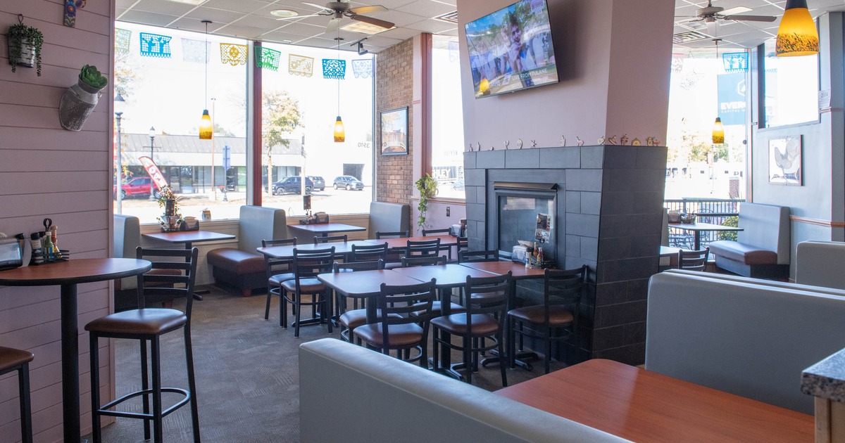 Interior of a restaurant with booths, tables, a fireplace, and colorful window banners