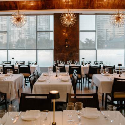 Elegant dining room with set tables and sun-shaped brass chandeliers.
