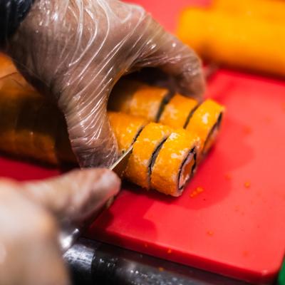 Chef using a knife to slice a sushi roll on a red cutting board.