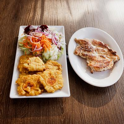 Grilled chicken breast served with fried plantains and a salad.