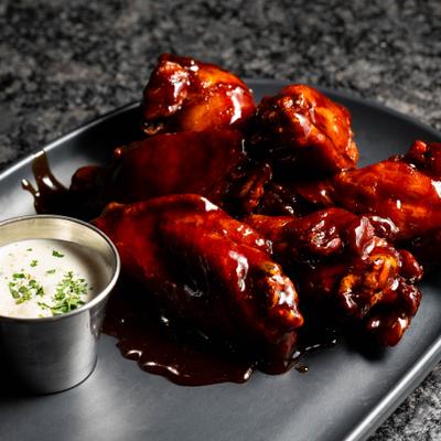 Chicken wings covered in red sauce served with a side of house ranch.