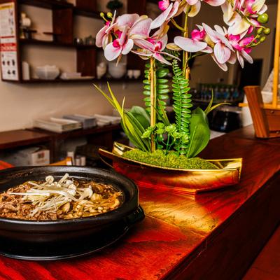 Savory hot pot dish served alongside decorative orchids on a wooden counter.