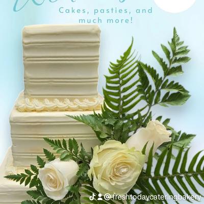 A smooth white cake, white roses and green ferns, set against light blue background.