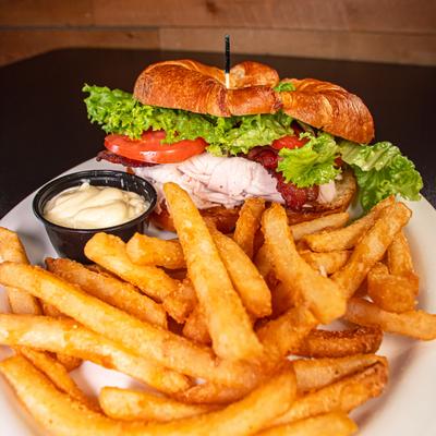Turkey club croissant served with fries and a dipping sauce.