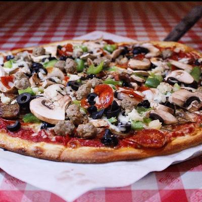 Supreme pizza loaded with various toppings served on a checkered tablecloth.