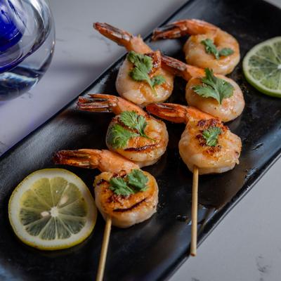 Two Shrimp skewers garnished with cilantro and lime wheels on a black plate.