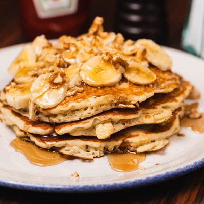 Pancakes drizzled with syrup and topped with sliced bananas and chopped walnuts.