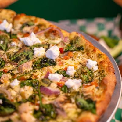 Pesto Supremo Pizza served on a metal tray, close-up.