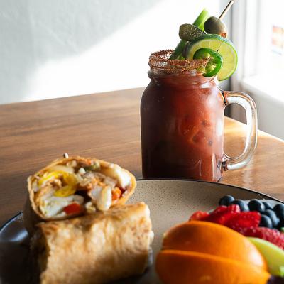 Breakfast burrito served with fresh fruit and bloody mary.