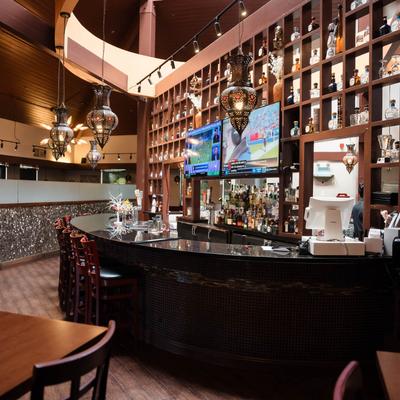 A curved bar with a granite countertop, twoTVs, and shelves stocked with bottles.