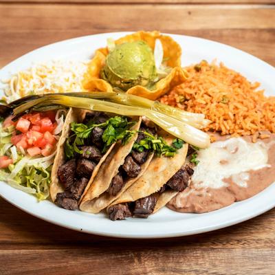 Steak tacos with rice, beans, cheese, and guacamole.