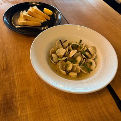 Steamed clams in savory broth, served with a side of toasted bread and a lemon wedge.