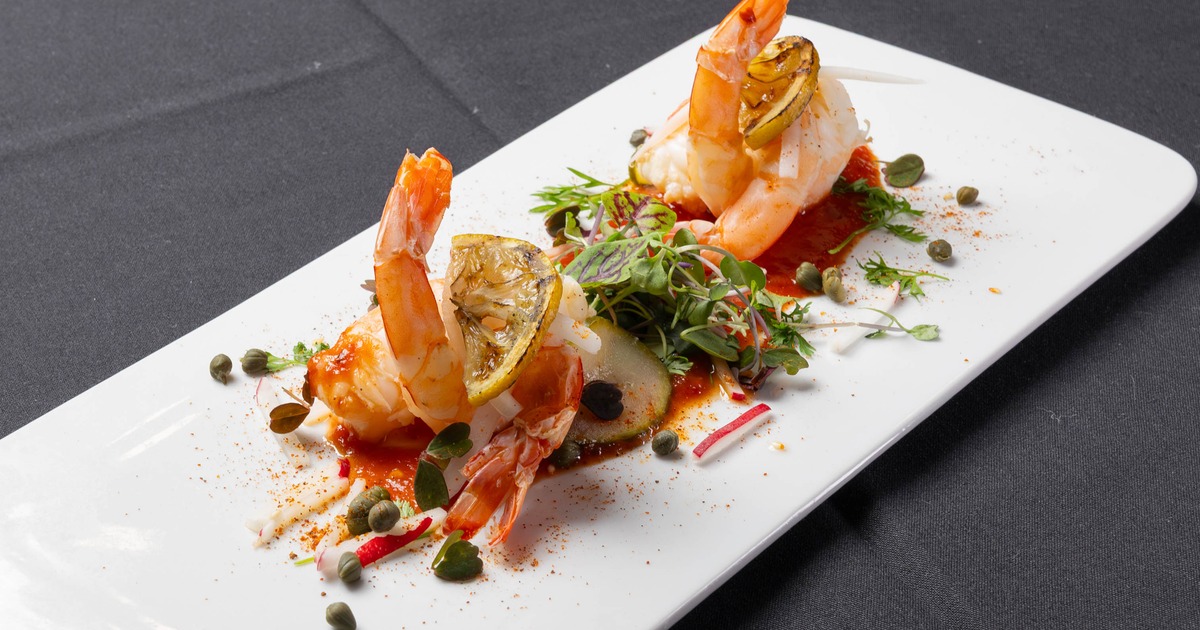Shrimp with lemon, capers, and red sauce served on a white platter