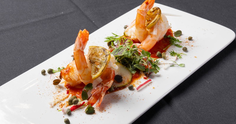 Shrimp with lemon, capers, and red sauce served on a white platter