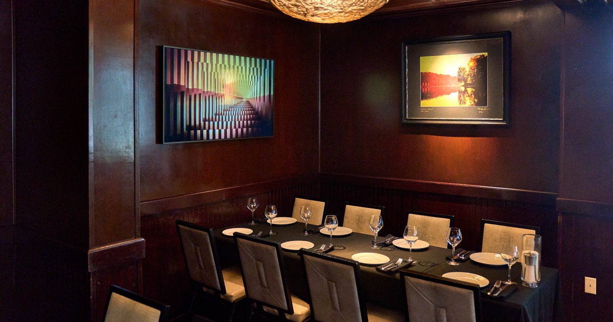 A dining area with a set table, cushioned chairs and framed artworks on the walls.