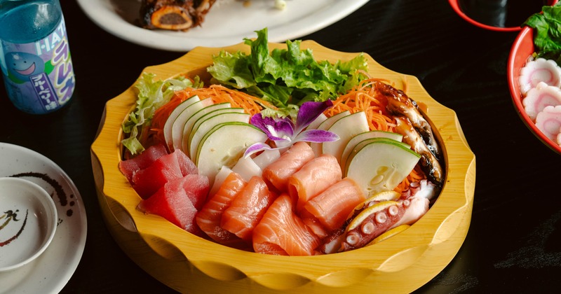 Fresh sashimi platter with raw fish, octopus, and vegetables in wooden bowl