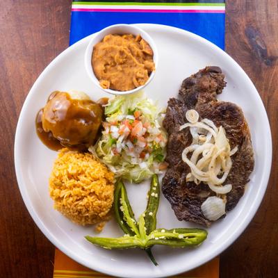 Grilled steak topped with grilled onion and served with traditional Mexican sides.