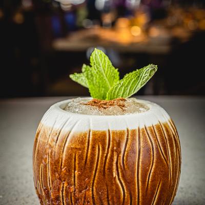 A mixed drink served in a coconut shaped tiki mug, garnished with mint leaves.